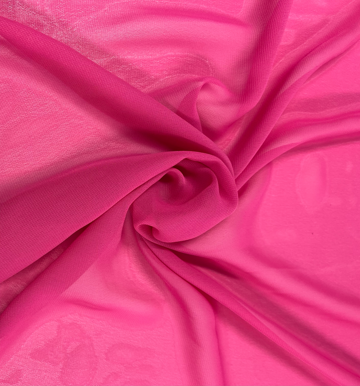 Close-up of the Hi-Multi Chiffon in hot pink, a fabric by Super Cheap Fabrics, elegantly arranged in a loose spiral. This 150cm wide polyester material forms a textured, swirling pattern. Its lightweight nature makes it appear soft and airy, with gentle folds and subtle shadows enhancing its delicate appearance.