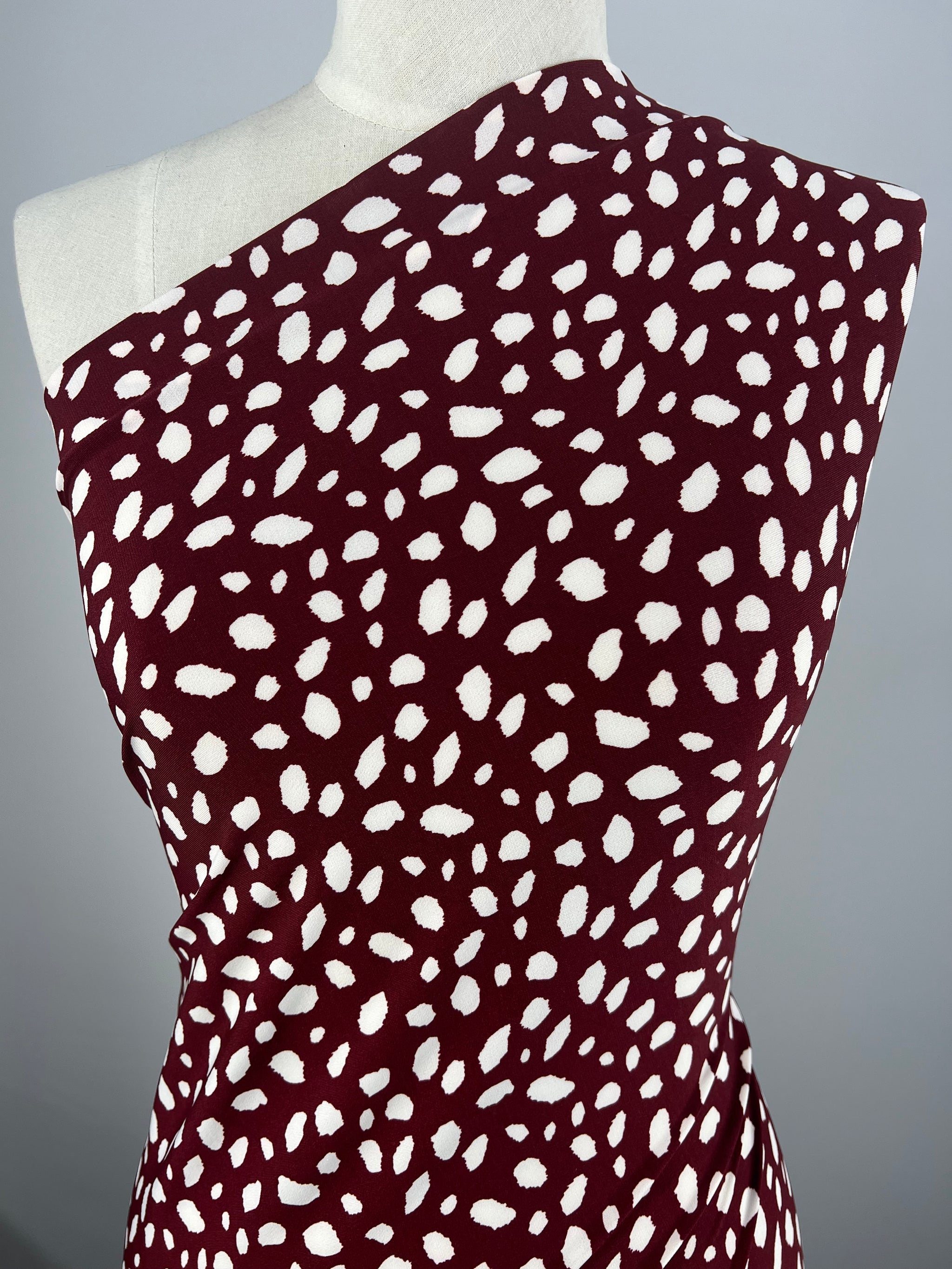 A mannequin showcases a chic and modern design with a maroon dress featuring a white abstract dot pattern created from the 