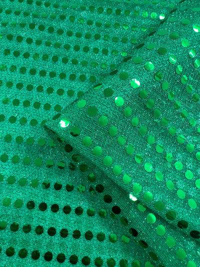 Close-up of Sequin - Emerald - 112cm from Super Cheap Fabrics, featuring shiny emerald sequins in a grid pattern on folded fabric, showcasing its sparkling, reflective texture—ideal for decorative projects and dancewear.