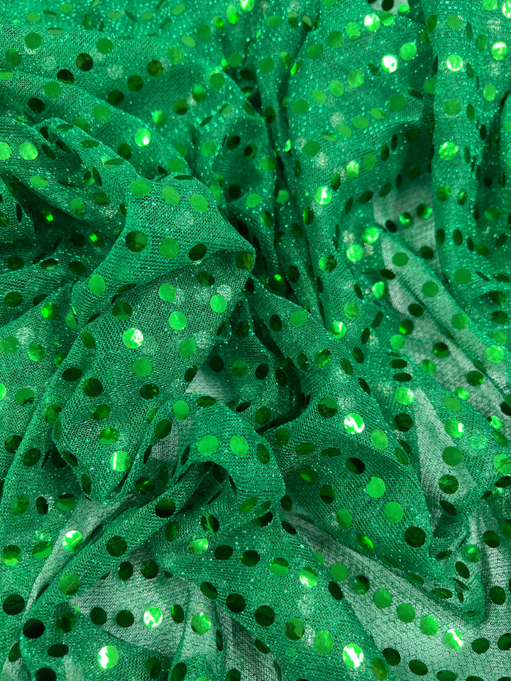 Sequin - Emerald - 112cm from Super Cheap Fabrics features vibrant green fabric with shiny emerald sequin polka dots. Its textured, crumpled surface reflects bright light, making the sequins sparkle brilliantly against the fabric.