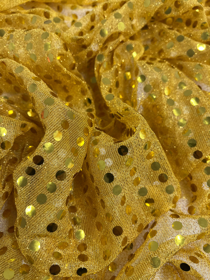 A close-up of Super Cheap Fabrics' Sequin - Gold - 112cm shows crinkled, lightweight gold fabric adorned with shiny round sequins, creating a vibrant, textured, and reflective surface.