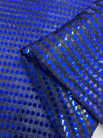 A close-up of Sequin - Sodalite Blue - 112cm by Super Cheap Fabrics shows shiny blue sequins in a grid on sheer dark mesh. Partially folded, it's perfect for dancewear and highlights texture and shimmer.