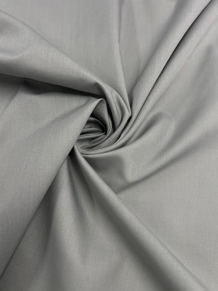 Super Cheap Fabrics' Poplin - Mirage Grey - 112cm features light gray poly cotton, gathered and twisted into a spiral at the center for soft folds and a smooth, lightweight texture.