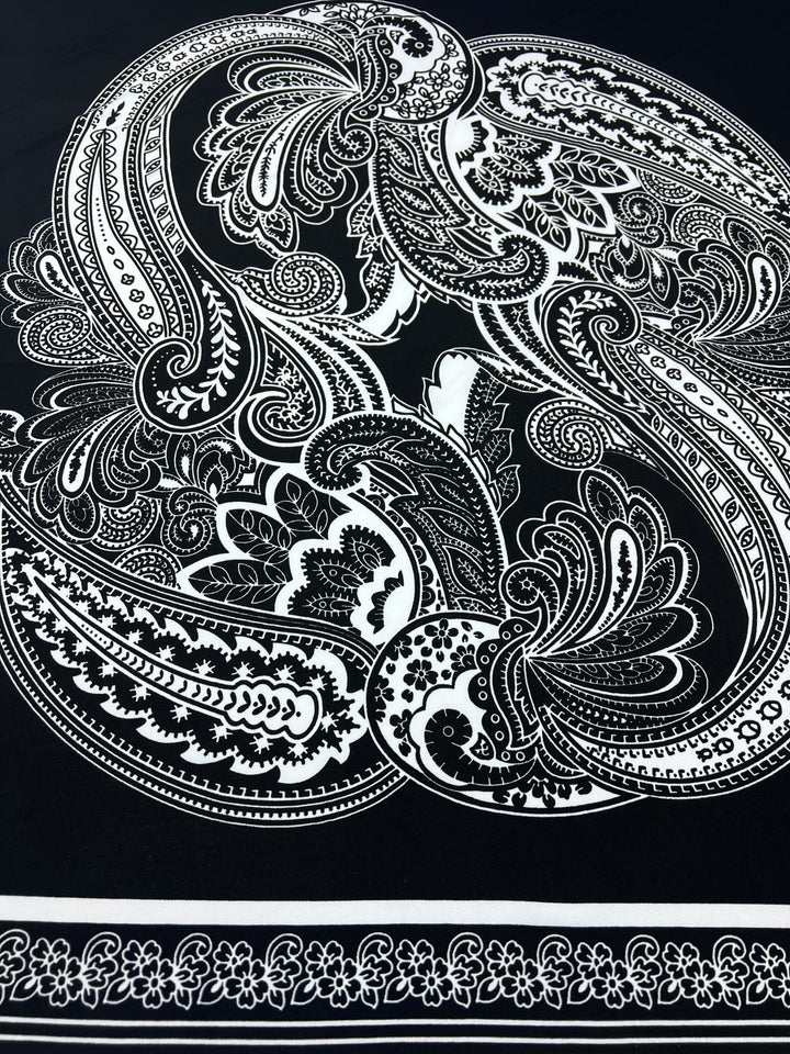 The Super Cheap Fabrics Printed Lycra - Antoinette Paisley 85cm Panel features intricate white paisley and floral prints on black, with a narrow border of small florals along the bottom edge.