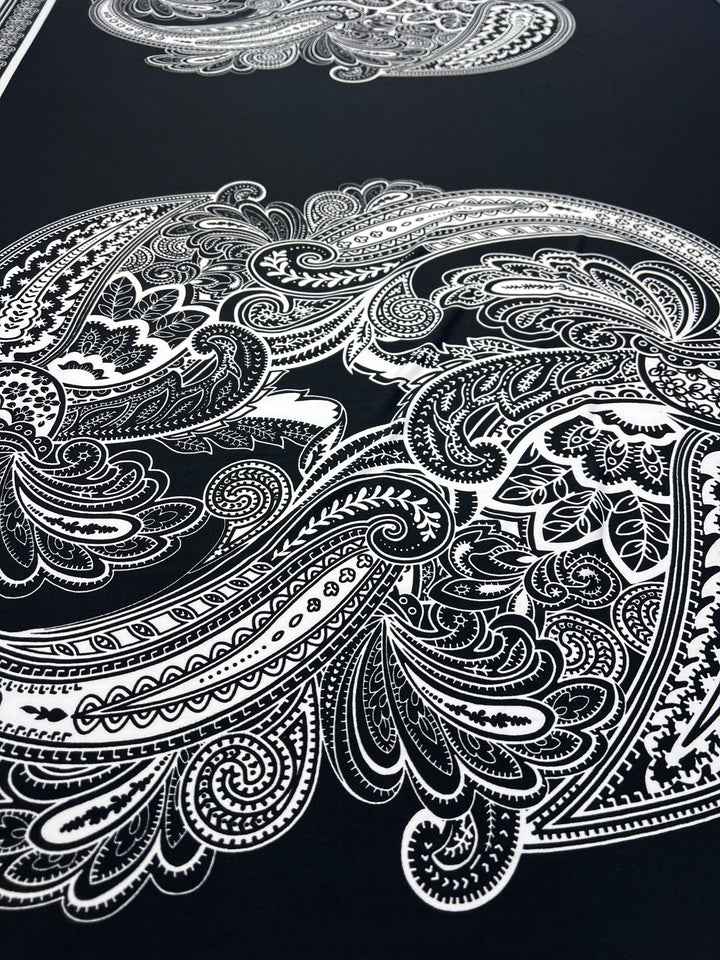 The Printed Lycra - Antoinette Paisley - 85cm Panel by Super Cheap Fabrics features intricate white paisley and floral patterns on dark medium-weight Polyester/Spandex, creating a bold, elegant look with swirling lines and delicate shapes.