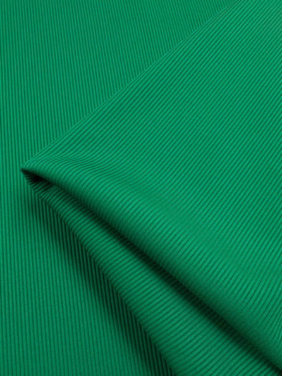 A close-up of the Rib Knit 1x1 - Lush Meadow by Super Cheap Fabrics reveals a vibrant green, medium-weight fabric with fine vertical lines and subtle shadows, suggesting softness and stretch. The neatly folded material appears smooth and well-crafted.