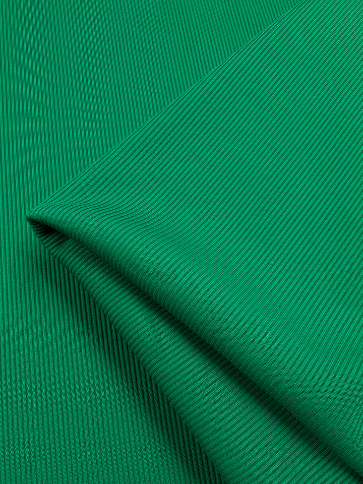 A close-up of the Rib Knit 1x1 - Lush Meadow by Super Cheap Fabrics reveals a vibrant green, medium-weight fabric with fine vertical lines and subtle shadows, suggesting softness and stretch. The neatly folded material appears smooth and well-crafted.