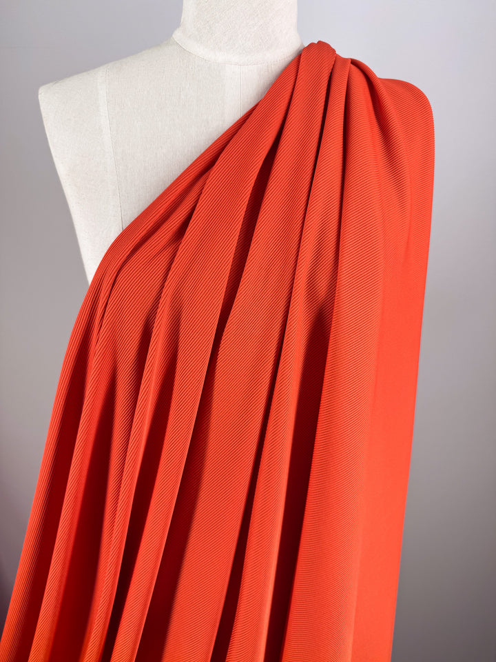The Rib Knit 1x1 - Tango from Super Cheap Fabrics is a bright red-orange stretch fabric with a subtle texture, elegantly draping over a dress form with soft folds at the shoulder and cascading smoothly down, ideal for flowy garments or drapery.