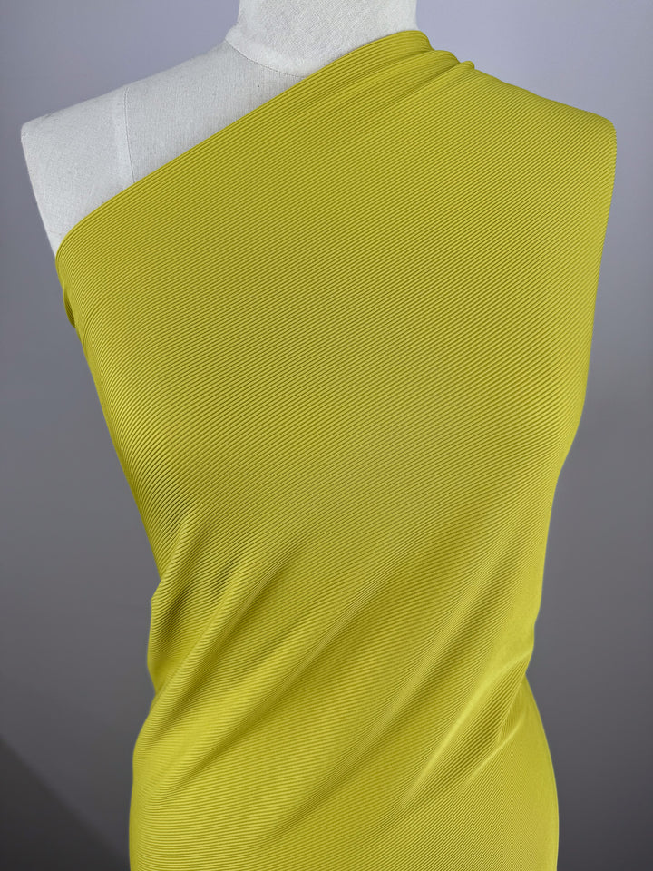 A dress form features Super Cheap Fabrics' "Rib Knit 1x1 - Squash - 127cm" in vibrant yellow, highlighting its medium weight texture and drape against a plain grey background, enhancing the fabric's vividness.