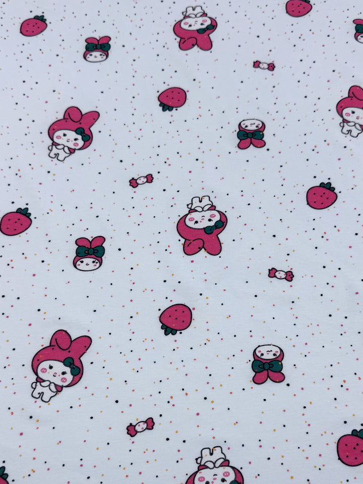The medium-weight Printed Jersey - Melody by Super Cheap Fabrics features cute cartoon characters with rabbit ears, strawberries, and candies on white. This 140cm fabric's two-way stretch is enhanced with pink, red, and green accents amid small colored dots.