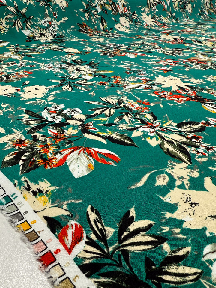 Super Cheap Fabrics' Printed Viscose - Tropic Bloom - 140cm is a green floral fabric with red, white, and cream flowers, dark leaves, and a color swatch strip of numbered samples along the edge. Designer deadstock from Prato, Italy.