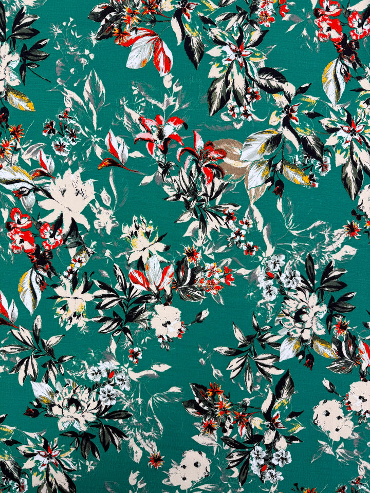 Super Cheap Fabrics’ Printed Viscose - Tropic Bloom - 140cm is a lively designer deadstock from Prato, Italy, featuring white, red, yellow, and black florals with green leaves on a teal background.