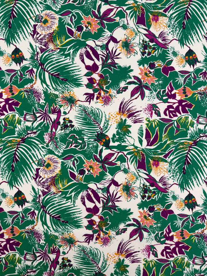 Printed Viscose - Jungle Orchid by Super Cheap Fabrics features a vibrant tropical floral pattern with green palm leaves, purple and pink flowers, and orange accents on white. This designer deadstock fabric from Prato, Italy measures 142cm wide.