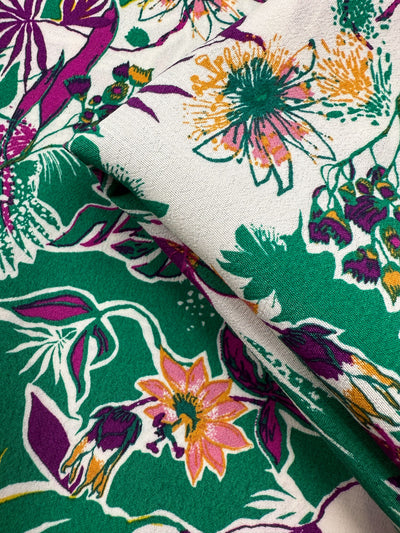 A close-up of Printed Viscose - Jungle Orchid by Super Cheap Fabrics reveals vibrant green, pink, purple, yellow, and white floral patterns with slight folds—crafted from designer deadstock fabric sourced from Prato, Italy.