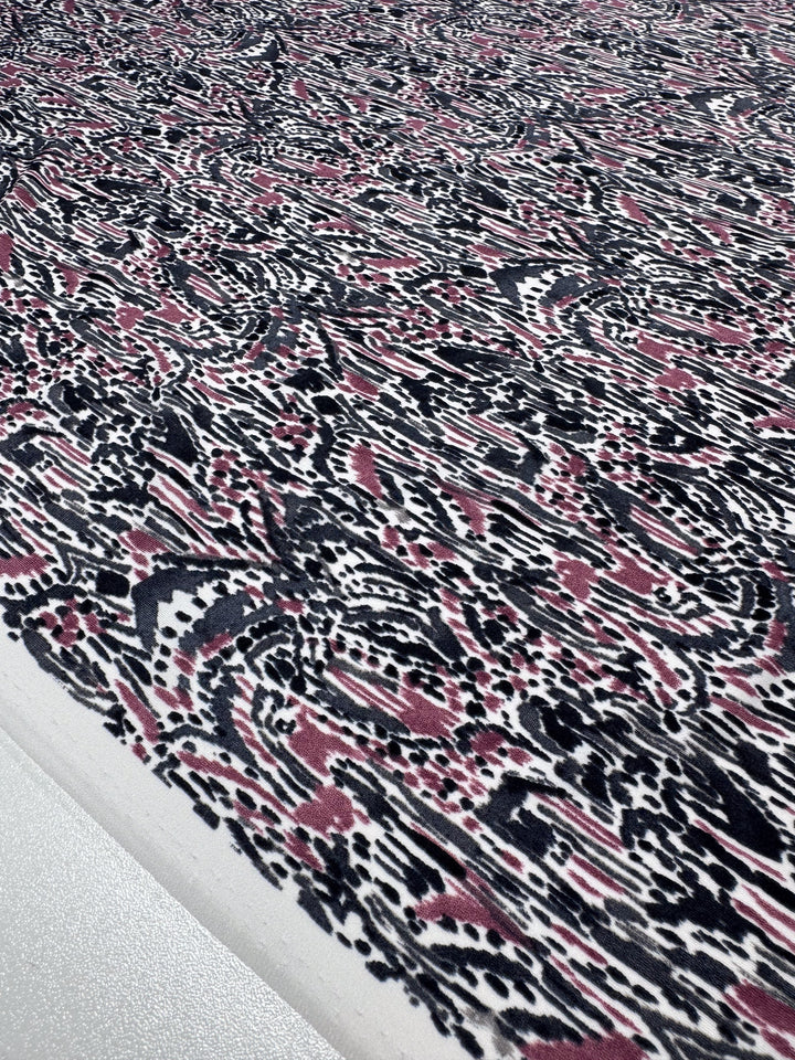 A close-up of Super Cheap Fabrics' Printed Lycra in Grey Musk highlights a medium-weight Polyester/Spandex blend with an abstract black, pink, and white pattern featuring dots, lines, and organic shapes for a dynamic texture. Product width: 150cm.