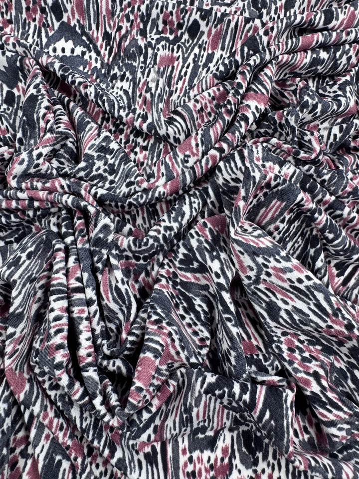 A close-up of the crumpled Printed Lycra - Grey Musk from Super Cheap Fabrics, showcasing an abstract pattern of irregular shapes and stripes in black, white, and pink on medium-weight fabric for a dynamic look.