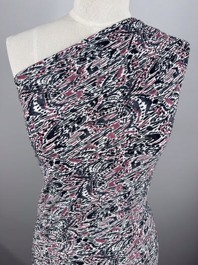 A mannequin showcases a one-shoulder dress made from Super Cheap Fabrics' Printed Lycra - Grey Musk (150cm), featuring a pink, black, and white abstract pattern with swirling geometric designs on a gray background.