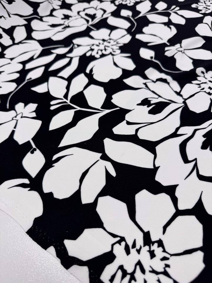 The Printed Jersey - Shadow Garden from Super Cheap Fabrics is a mid-weight polyester with a stunning black and white floral design, featuring large white flowers and leaves on a bold black background. Ideal for versatile clothing use. Width: 150cm.