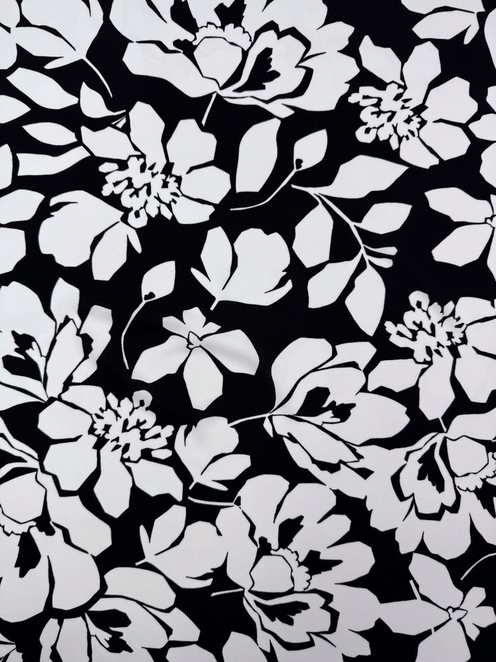 The "Printed Jersey - Shadow Garden - 150cm" from Super Cheap Fabrics features a black and white floral pattern with various flower and leaf sizes on mid-weight polyester, creating an intricate design ideal for clothing material.