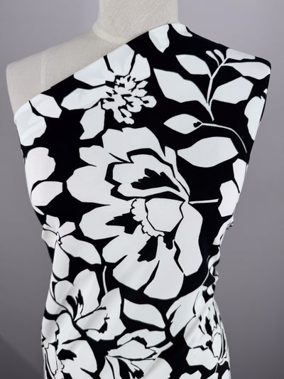 Close-up of a mannequin showcasing Super Cheap Fabrics' Printed Jersey - Shadow Garden. This black and white floral patterned polyester fabric, sized 150cm, features large motifs with contrasting leaves and petals diagonally wrapped across the bust against a neutral background.