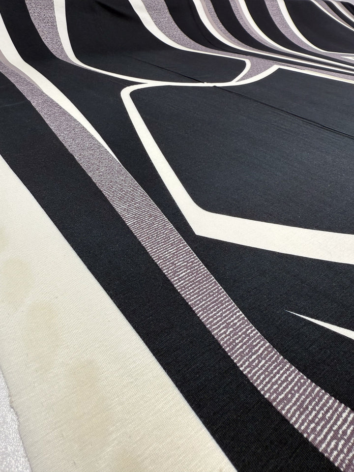 A close-up of Super Cheap Fabrics' Viscose Knit - Curve - 145cm shows bold black, white, and taupe geometric stripes with angular and curved lines for a modern, abstract look.