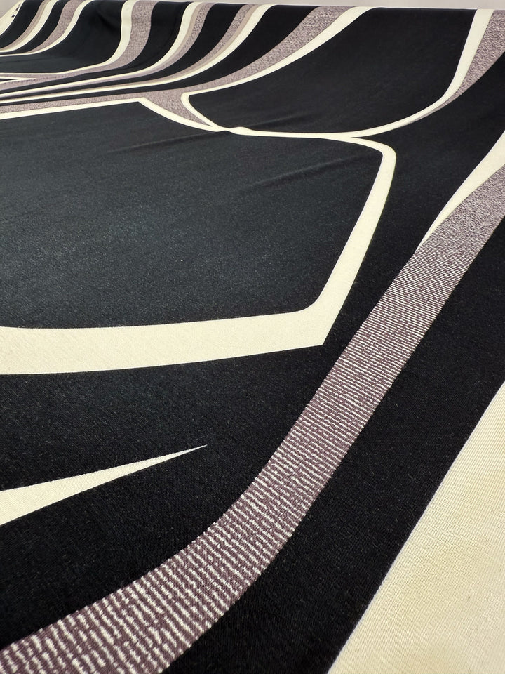 A close-up of Super Cheap Fabrics' Viscose Knit - Curve - 145cm shows bold black, cream, and light brown geometric patterns with curved and angular lines on a stretchy, breathable surface.