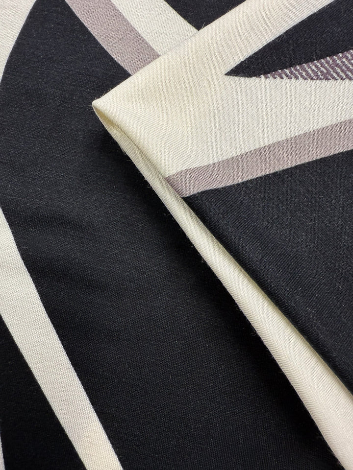 Close-up of Super Cheap Fabrics' Viscose Knit - Curve (145cm): two overlapping breathable stretch fabrics with abstract black, white, and taupe geometric angular patterns.