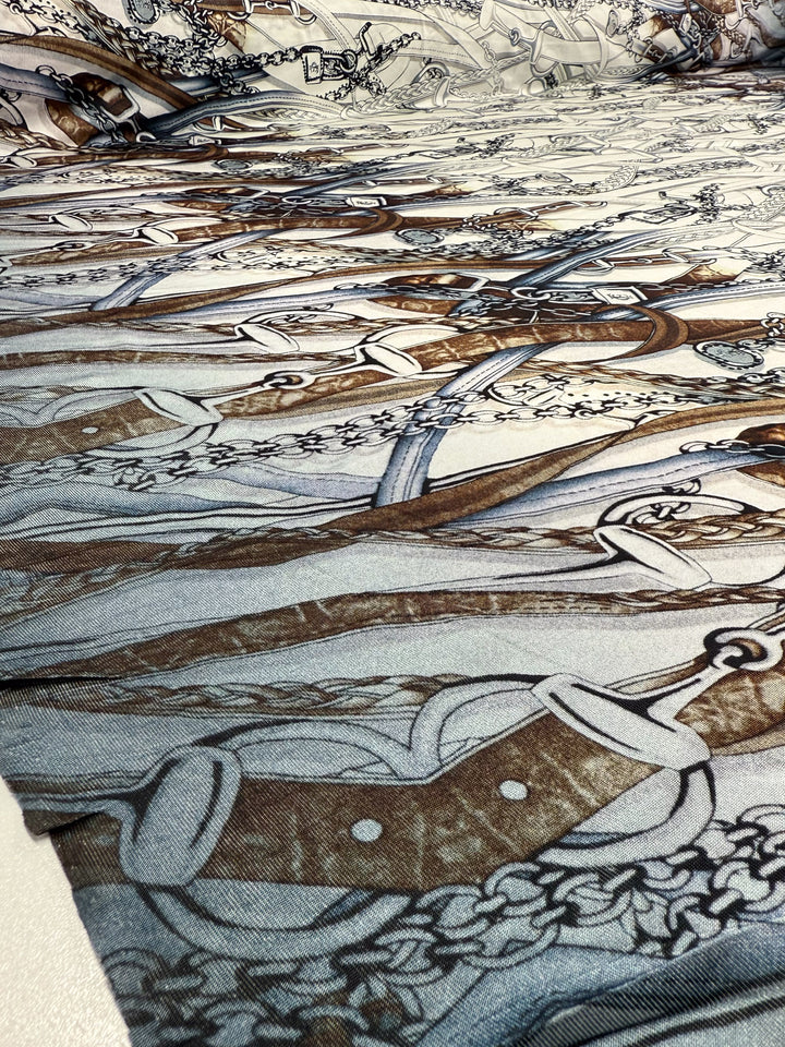 A close-up of Super Cheap Fabrics' Viscose Knit - Link (138cm) shows its intricate overlapping pattern of swords, ornate handles, and chains in brown, gray, and black on stretch fabric.