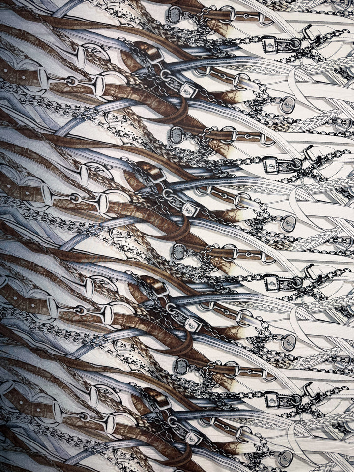 Super Cheap Fabrics' Viscose Knit - Link (138cm) features an intricate equestrian-themed pattern with brown leather bridles, bits, and chains overlapping on a white stretch fabric.