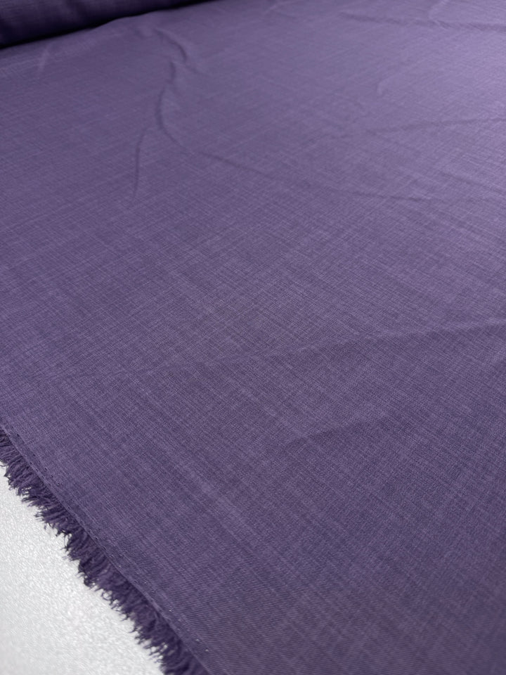 A close-up of Super Cheap Fabrics' Twill Suiting - Wineberry (150cm) shows its smooth texture, subtle wrinkles, and a small fringed border at the edge that highlights its versatile use for fashion projects.