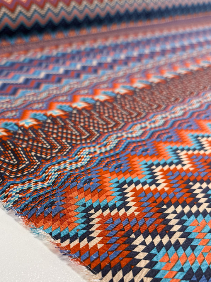 Close-up of Printed Viscose - Zulu by Super Cheap Fabrics, featuring colorful zigzag and diamond patterns in red, blue, orange, and cream tones, with intricate geometric designs across its 150cm width.