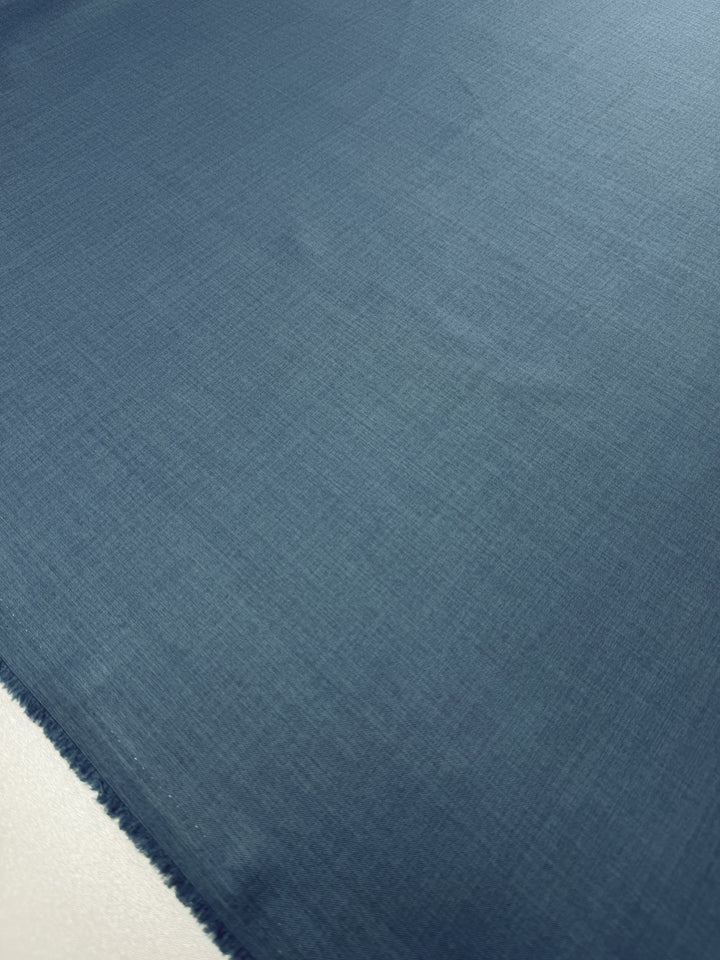 A close-up of Super Cheap Fabrics’ Twill Suiting - Bluesteel - 150cm, laid flat to show its smooth, subtly textured surface and slightly frayed edges in the lower left corner.