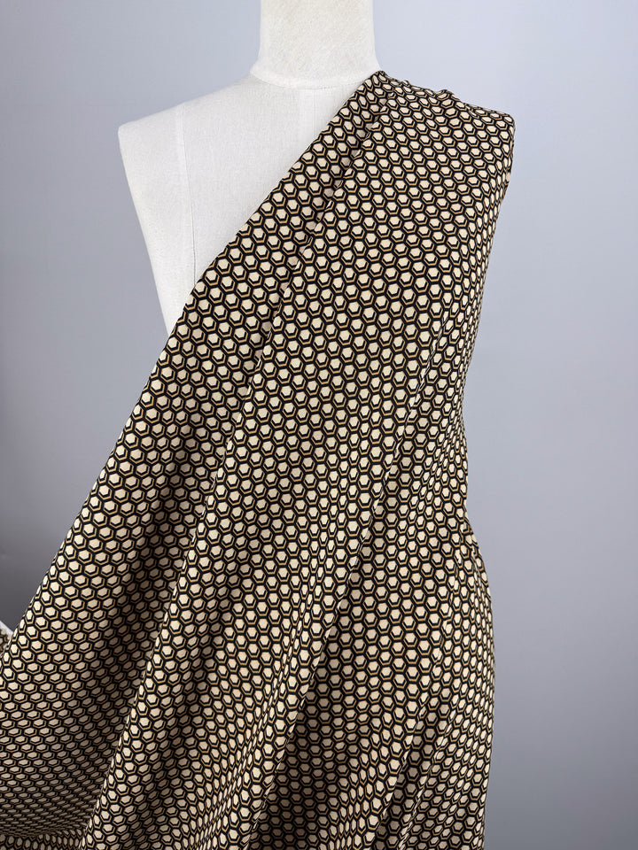 A mannequin displays Super Cheap Fabrics' Printed Viscose - Hive (145cm), featuring a black fabric with a repeating pattern of small beige circles, set against a plain light gray background.