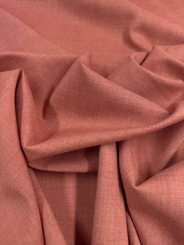 A close-up of Super Cheap Fabrics’ Twill Suiting - Terra Cotta (150cm) shows its soft texture, pinkish-coral hue, and visible diagonal weave, draped in gentle folds and creases.