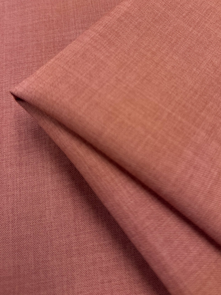 A close-up of Super Cheap Fabrics' Twill Suiting - Terra Cotta (150cm) shows its soft, textured surface and subtle diagonal weave. The 100% polyester fabric is displayed folded on a matching background.