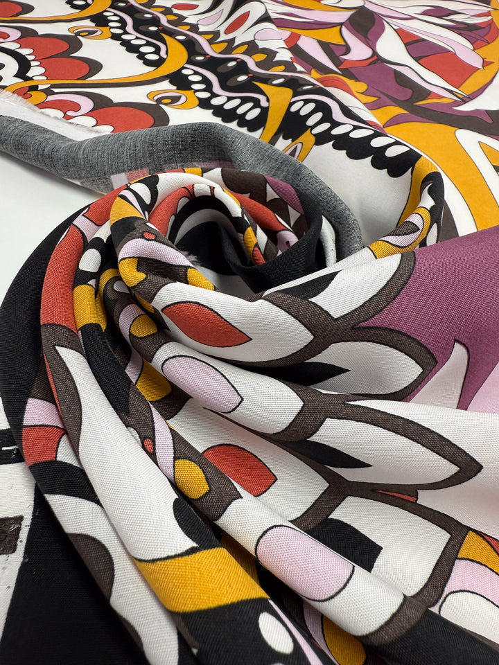 A close-up of Printed Viscose - Fantasia by Super Cheap Fabrics, featuring vibrant swirling patterns in yellow, red, pink, black, and white on 145cm wide Italian fabric, partially rolled to showcase its colorful design.