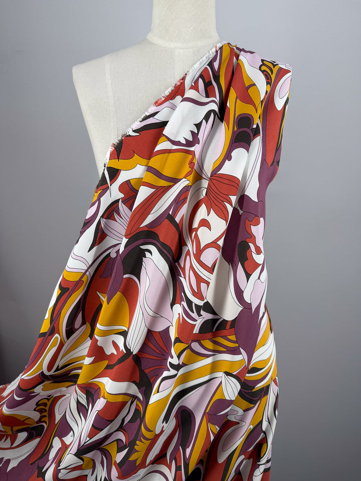 A mannequin displays Super Cheap Fabrics' Printed Viscose - Fantasia (145cm), featuring a lightweight, retro-inspired abstract print with swirls of red, yellow, pink, black, and white on light gray.