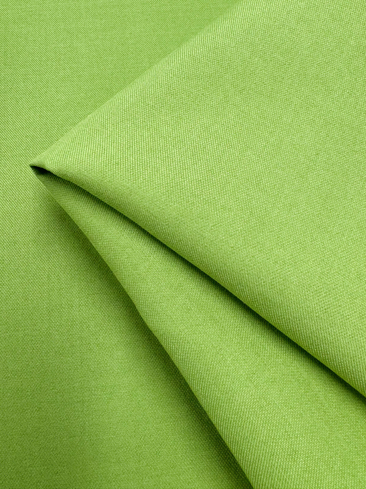 A close-up of Super Cheap Fabrics’ Twill Suiting - Green Glow (150cm), neatly folded to showcase its smooth polyester texture and fine diagonal weave, with soft diagonal lines formed by the fabric’s folds.
