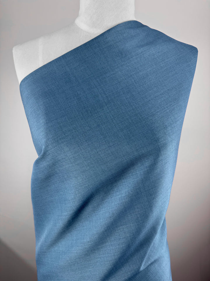 A white mannequin displays Super Cheap Fabrics' Twill Suiting - Bluesteel (150cm), draped smoothly across one shoulder and diagonally over the torso, set against a softly lit, plain background.