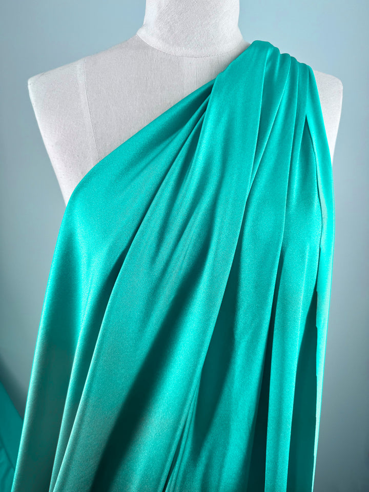 A white mannequin displays Super Cheap Fabrics' Nylon Lycra - Columbia (154cm) in bright turquoise, styled elegantly one-shoulder against a light blue background—ideal for chic swimwear projects.