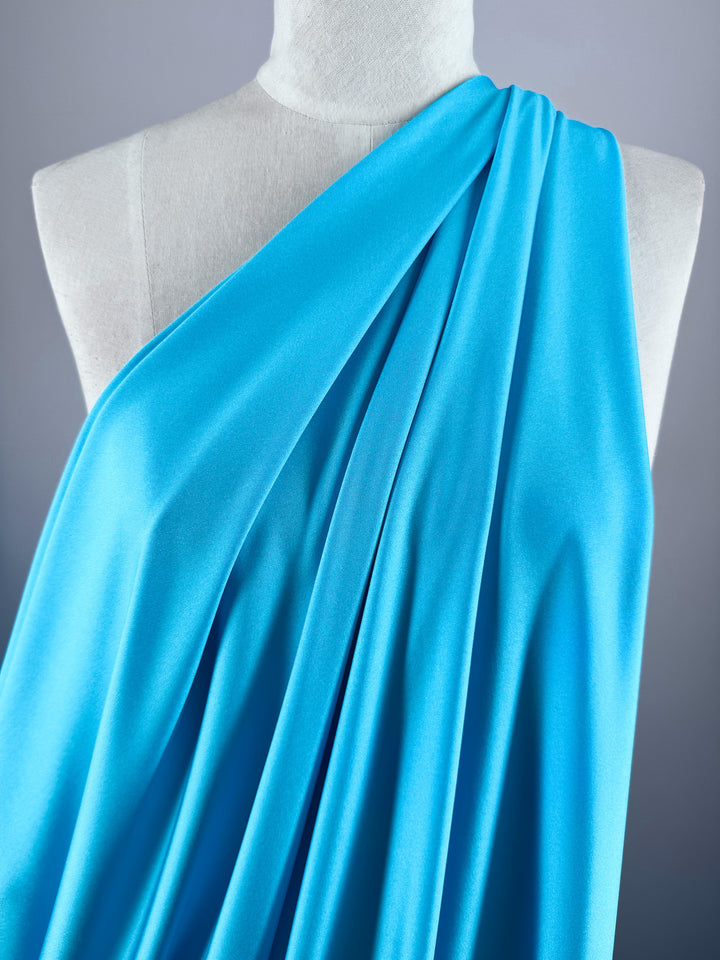 A white mannequin displays Super Cheap Fabrics’ Nylon Lycra - Blue Atoll (154cm), a smooth, bright blue fabric with soft folds and four-way stretch, set against a plain light gray background.