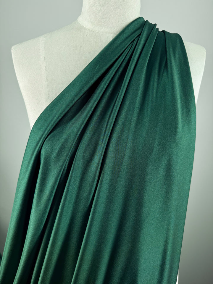 A mannequin showcases Super Cheap Fabrics’ Nylon Lycra - Dark Green - 154cm, draped over one shoulder. The smooth, four-way stretch fabric creates elegant folds—perfect for stylish swimwear—against a neutral background.