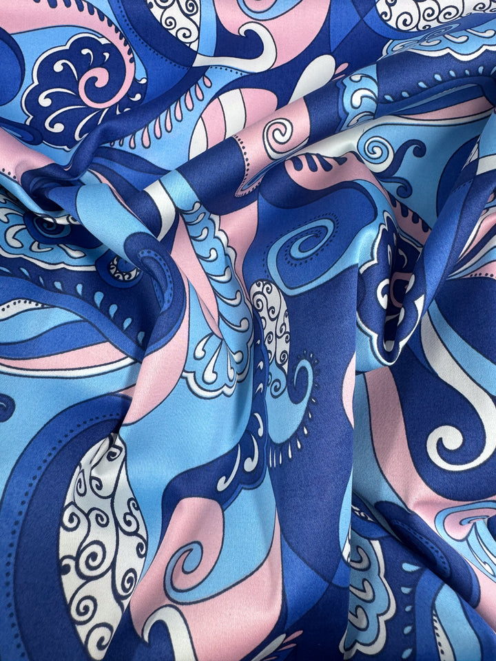 A close-up of Serenity Waves by Super Cheap Fabrics shows swirling blue, pink, white, and navy patterns on lightweight cotton sateen (148cm wide) with a silky texture—ideal for multiuse projects.