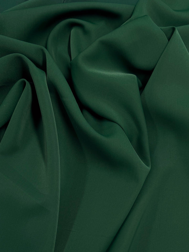 A close-up of Super Cheap Fabrics' Microfibre Suiting in Dark Green (150cm) shows soft folds and drapes, highlighting the smooth, textured look of this lightweight polyester material.