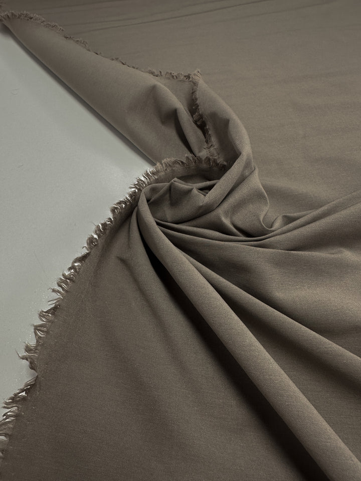 A close-up of draped "Moon Rock" Lightweight Bengaline by Super Cheap Fabrics, showcasing a smooth, dark olive texture. The slightly frayed edges add rustic charm as the 152cm fabric's gentle folds create subtle shadows and highlights.