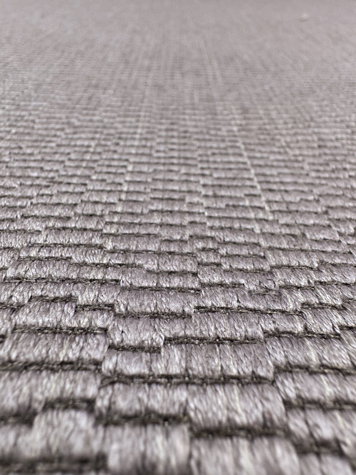 Close-up of Oscar Dusk Upholstery Jacquard by Super Cheap Fabrics, 142cm wide. This heavy-weight fabric features a textured, grid-like woven pattern in light gray with a subtle sheen, highlighting its depth and quality.