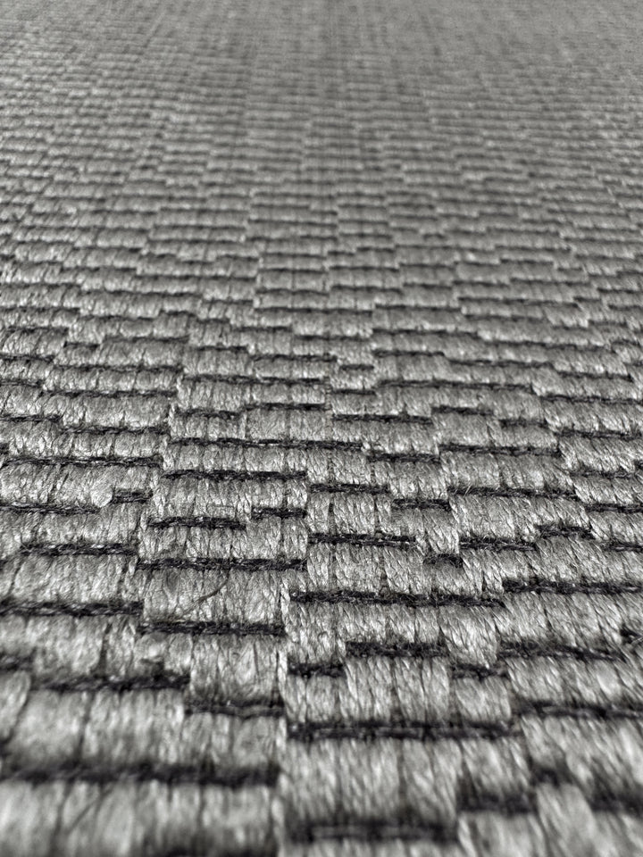 Close-up of Super Cheap Fabrics' Upholstery Jacquard - Oscar Putty (148cm), featuring a textured gray grid-like woven pattern with a subtle raised, brick-like look; sharply focused in front, blurring toward the back.