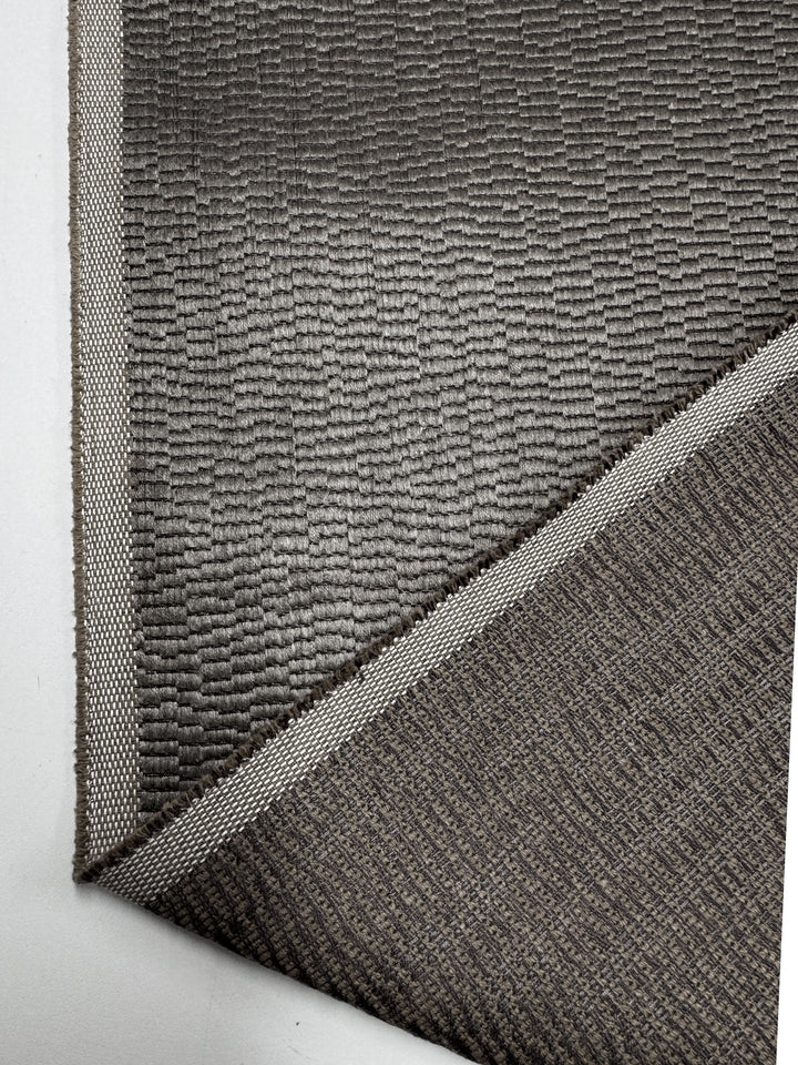 A close-up of Super Cheap Fabrics’ Upholstery Jacquard - Oscar Putty (148cm) shows its textured, grid-like woven pattern with a visible border, made from heavyweight fabric and revealing the edge and underside.