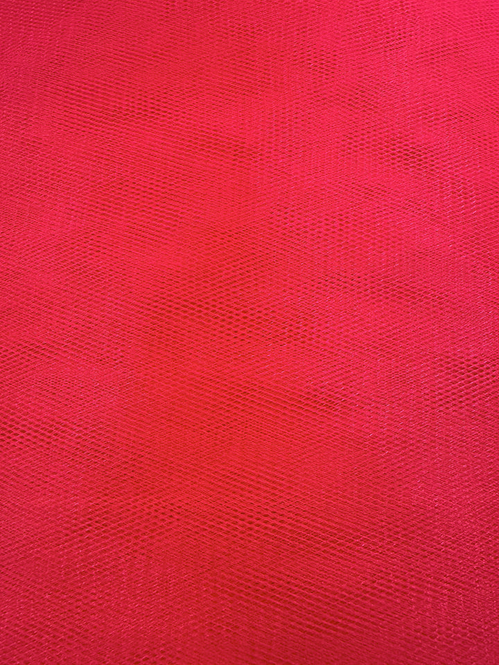Close-up of Soft Tulle - Teaberry by Super Cheap Fabrics, 150cm wide. The textured red surface features a subtle diamond mesh pattern, and lighting highlights the airy, lightweight quality typical of tulle fabric.