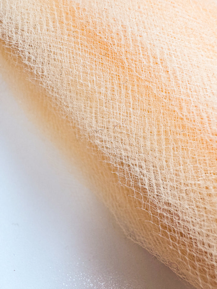 Close-up of Super Cheap Fabrics’ Soft Tulle - Peach - 150cm, showcasing its light beige net-like texture on a white surface—perfect for bridal veils and sheer, lightweight projects.
